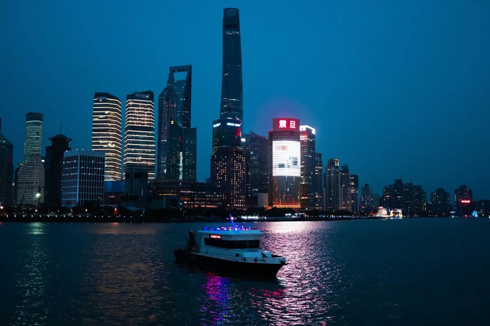 The Shanghai Pudong skyline lit up at dusk, with a boat crossing the Huangpu river